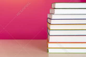 Stack of colorful books, bright colorful pink background, free copy space. Books on table, no labels, blank spine. Back to school