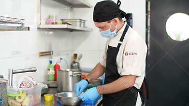 Cooking. man chef, in protective gloves and a mask, prepares food in kitchen, in canteen. health food and safety concept