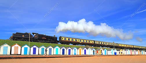 Steam train passing colorful beach huts