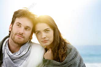 Young couple sitting on summer beach with blanket