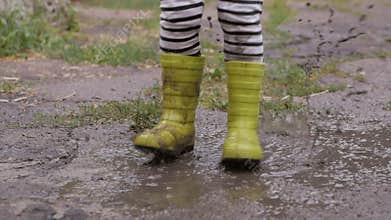 A small child shod in rubber boots, jumping in a dirty puddle after the rain.