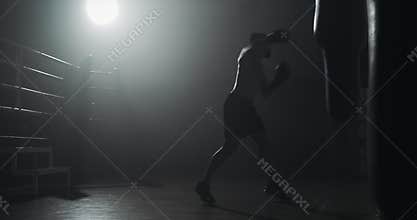Silhouette boxer man hits punching bag in dark gym. Fighter workout. Male boxer exercising in dark. Kickboxer silhouette