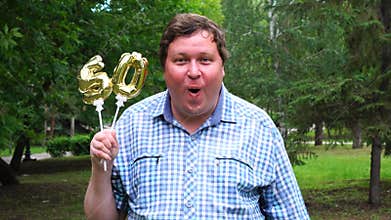 Big man holding golden balloons making the 50 number outdoor. 50th anniversary celebration party
