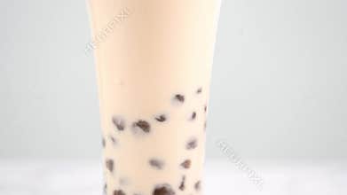 Stirring tapioca pearl bubble milk tea in drinking glass, tasty taiwanese popular drink on bright marble table. Homemade concept.