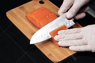 Hands cooks close-up. The chef cuts with a knife a red fish, smoked salmon on a wooden cutting board.