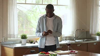 Happy african man using smartphone mobile apps cooking in kitchen