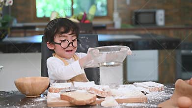 Cute little Asian boy sifting dough flour with sifter sieve colander in home kitchen for prepare to baking bakery and cake. Thai k