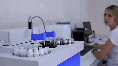 Automatic biochemical analyzer machine in medic lab and woman works on computer.