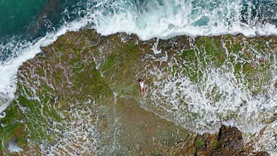 AERIAL VIEW. Sea waves splashing with foam and spray to stony coast. Beautiful woman lies on rocky beach.