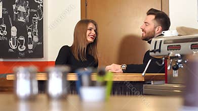 The couple sits in a coffee shop behind the bar and drinks cappuccino.