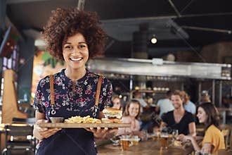Portrait Of Waitress Serving Food To Customers In Busy Bar Restaurant