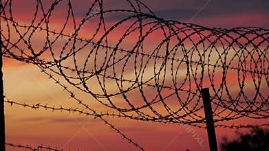 The fence with barbed wire on the background of a cloudy red-blue sky.