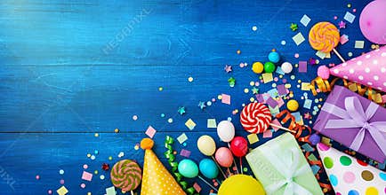 Holiday background with balloons, gift boxes and confetti. Birthday and party supplies on blue table top view. Banner format