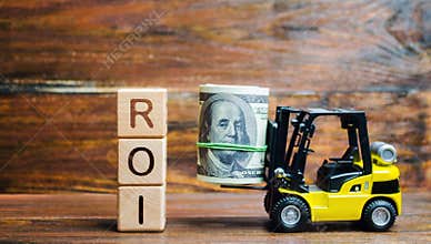 Wooden blocks with the word ROI and money with forklift. Ratio between the net profit and cost of investment resulting from an