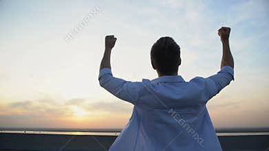 Back view of Caucasian man raising hands to sky on sunset background, motivation