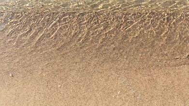 Sea wave with white foam running on a sandy shore, and going back, clear water close up video