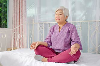Keep calm and breath. Senior woman meditating in lotus position on bed at home, Healthy morning routine and meditation concept