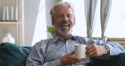 Happy senior man drinking tea on sofa looking at camera