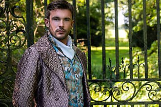 Portrait of handsome gentleman dressed in vintage costume standing in stately home courtyard with railings in background