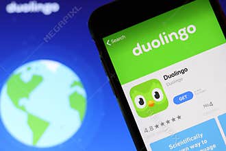 Mobile phone with Duolingo icon on screen close up with website on laptop. Blurred background with Duolingo logo