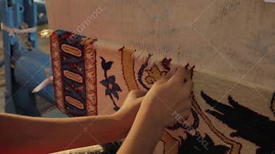 A woman sews an oriental carpet. Close-up of hands work behind a loom