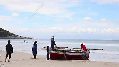 Local fishermen attending to their small fishing boat on fish hoek beach Cape Town
