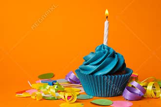 Delicious birthday cupcake with blue cream and candle on orange background