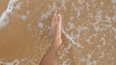 Point of view of young man stepping at the golden sand at sea beach. Male legs walking near ocean. Bare foot of guy