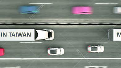 Aerial overhead view of trailer trucks with MADE IN TAIWAN text driving along the road. Taiwanese business related