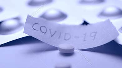 White pill tablet falling into paper with the text COVID-19 in slow motion. Corona virus flu dose of medicine