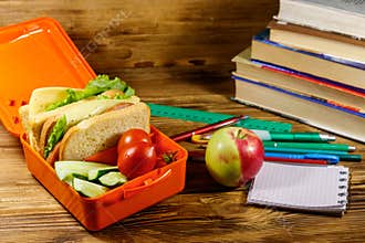 Back to school concept. School supplies, books, apple and lunch box with sandwiches and fresh vegetables on wooden desk