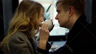 Couple on a date in cozy cafe, talking, drinking coffee from one cup and having fun together