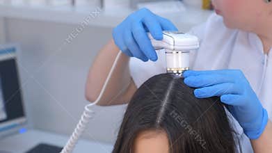 Doctor trichologist examines woman patient`s hairs using dermatoscope in clinic.
