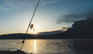 Fishery concept, outline fishing rod at sunrise sunlight, hobby sport on mist evening lake, catch fish on river on background nigh