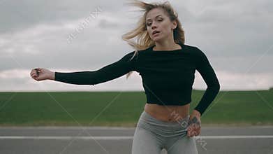 Hot girl is dancing outdoor at the road background. Sexy blonde woman is practicing dance