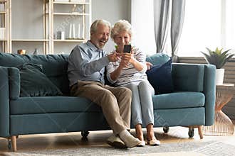 Excited 60s couple sit on couch making selfies on cellphone