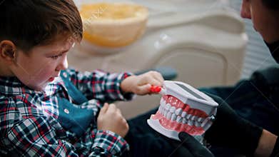 A little boy having a treatment in the dentistry - the kid brushing teeth on the jaw model