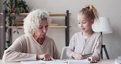 Happy old grandmother helps cute school kid granddaughter with homework