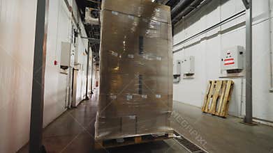 Worker carries cardboard on forklift truck along storehouse
