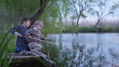 Relationship, friendly boy brothers catch fish on a wooden fishing rod sitting on the boards by the pond in the middle