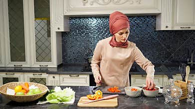 Woman in hijab stands at kitchen table cutting vegetable