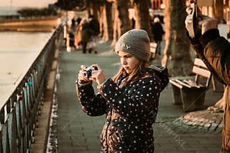 Young caucasian girl taking photo of the sunset at the border of a sea