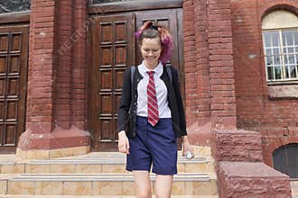Female student teenager in uniform with backpack, building school background