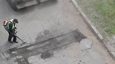 Road worker cleans old asphalt with blower for laying new asphalt, road repair, industry