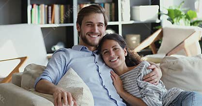 Smiling young couple hugging on comfortable couch looking at camera
