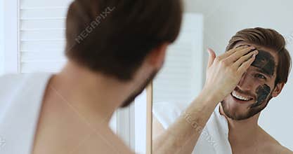 Young man applying black charcoal clay mask.