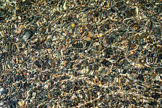 The texture of the bottom. Many small stones are visible under the clear water. Water ripples of the sea, sun rays on