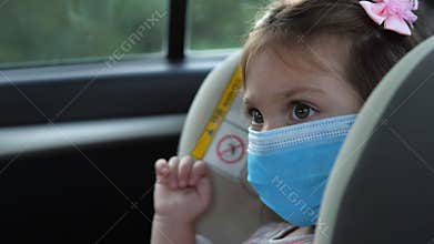 Little girl in a medical mask is sitting in a child seat in the car. Covid-19 Coronavirus pandemic global spread concept