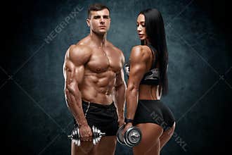 Sporty couple workout with dumbbells. Muscular man and woman showing muscles