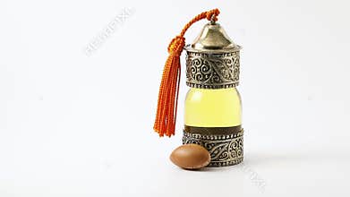 Single argan nut is rolling towards a bottle of Argan Oil